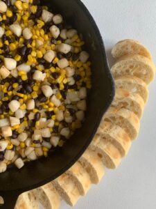 scallop corn succotash in cast iron skillet with sliced french bread on the side.