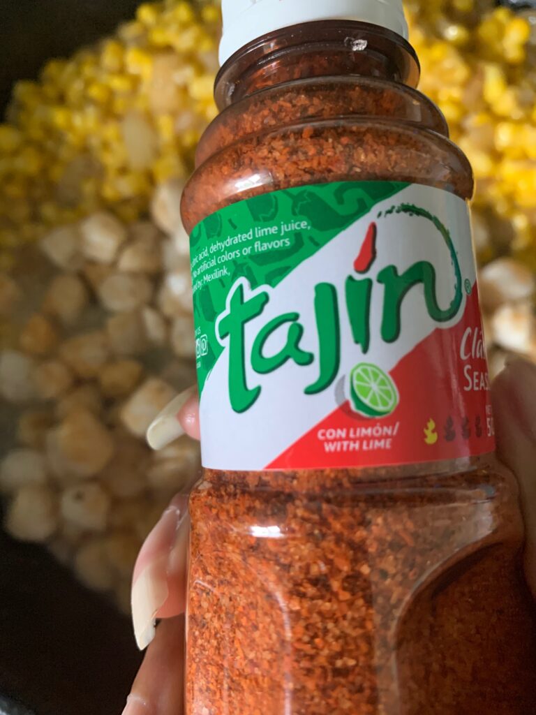tajin seasoning shown held over scallop corn succotash.